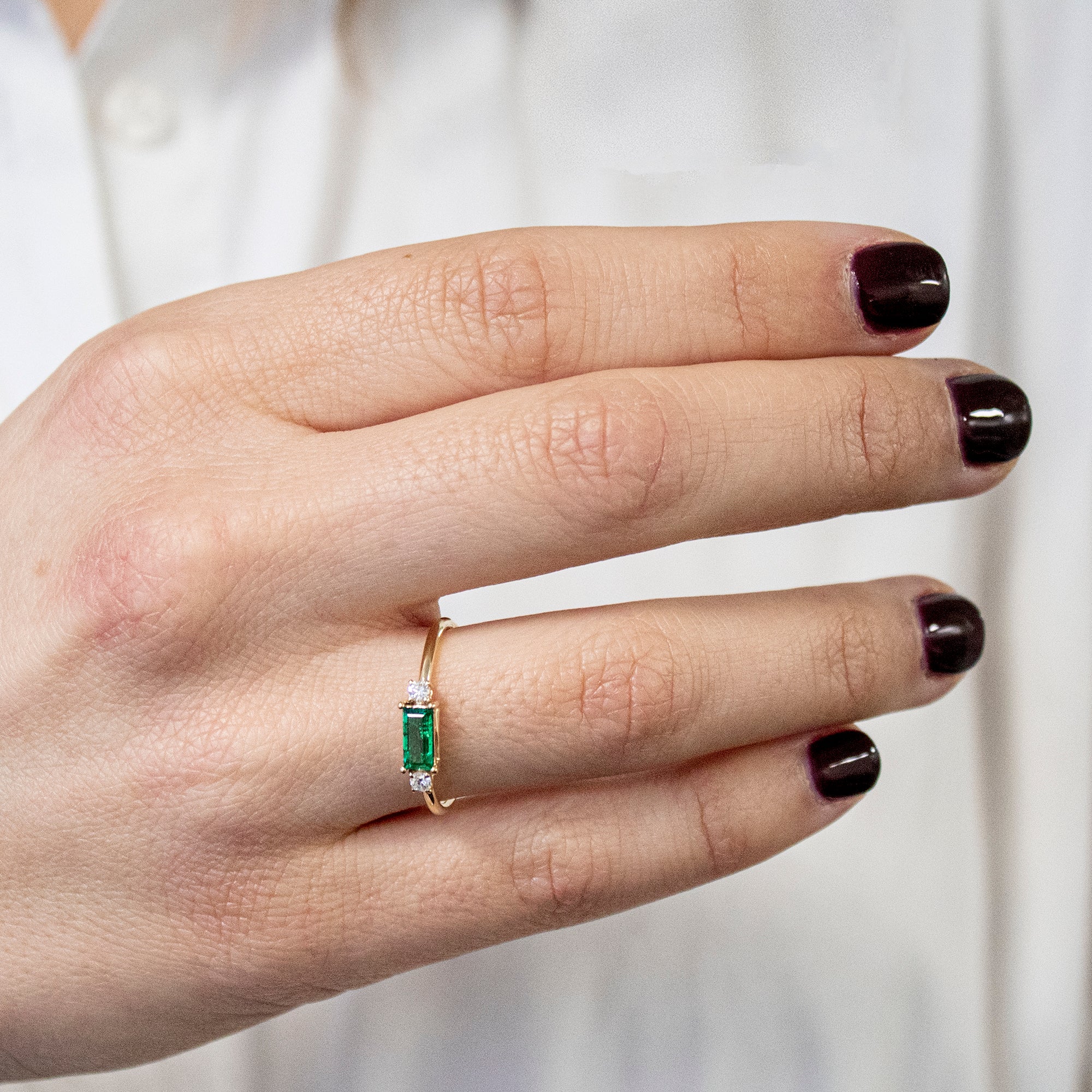 Anillo oro 18K trilogía de esmeralda y diamantes en la mano de una mujer