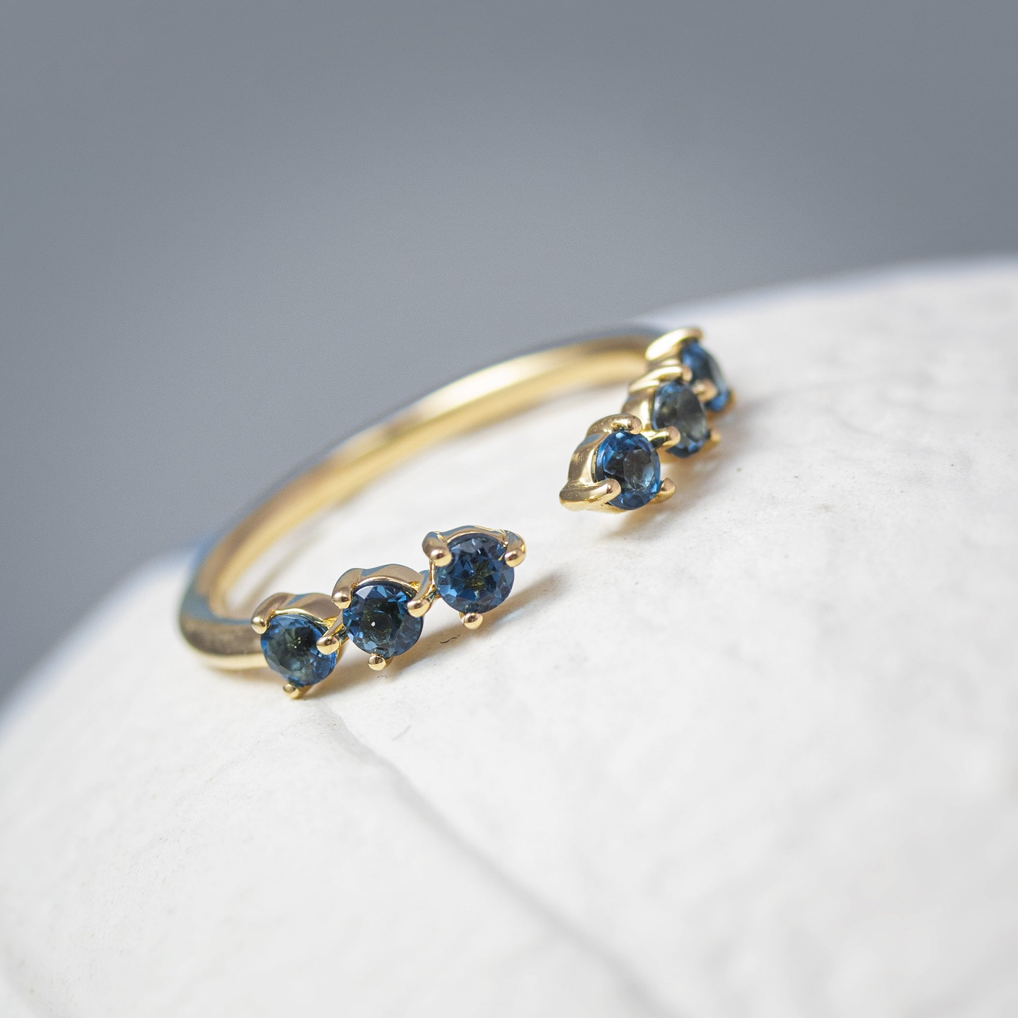 Anillo abierto en oro 18k con 6 topacios en azul en fondo blanco